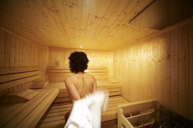 Eine Frau ist auf dem Weg in die Sauna und zieht sich dabei den Bademantel aus. | © Hotel Eggerhof