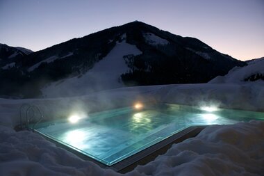Beheizter und beleuchteter Außenpool bei Nacht, im Hintergrund sind die Konturen der Bergwelt zu erkennen. | © Hotel Eggerhof