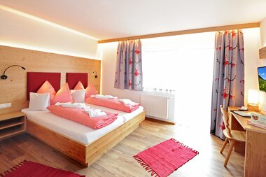 Helles Zimmer mit einem Doppelbett, einer Sitzgelegenheit sowie einem Schreibtisch und einen Zugang zum Balkon | © Hotel Eggerhof