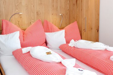 Doppelbett mit einer rot-weiß karierten Bettwäsche, zusätzlich Zirben und Heupolster | © Hotel Eggerhof