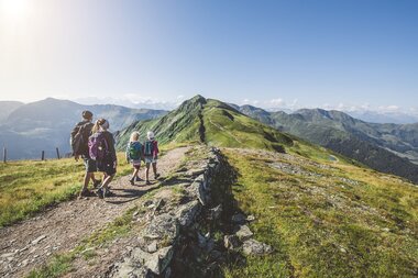 Hiking with the family in Saalbach along a mountain ridge under a bright blue sky. | © saalbach.com